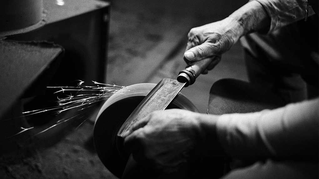 A blacksmith sharpening a traditional blade on a grinding wheel with sparks flying.